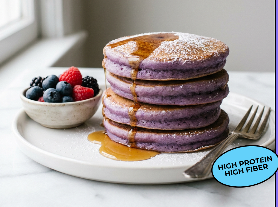 A stack of purple taro protein pancakes with syrup and a bowl of berries