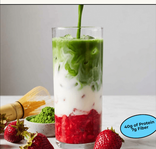 A layered strawberry matcha latte in a tall glass with a matcha whisk and fresh strawberries